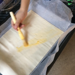 Laat je kind het bladerdeeg uitrollen op een bakpapier en insmeren met eigeel